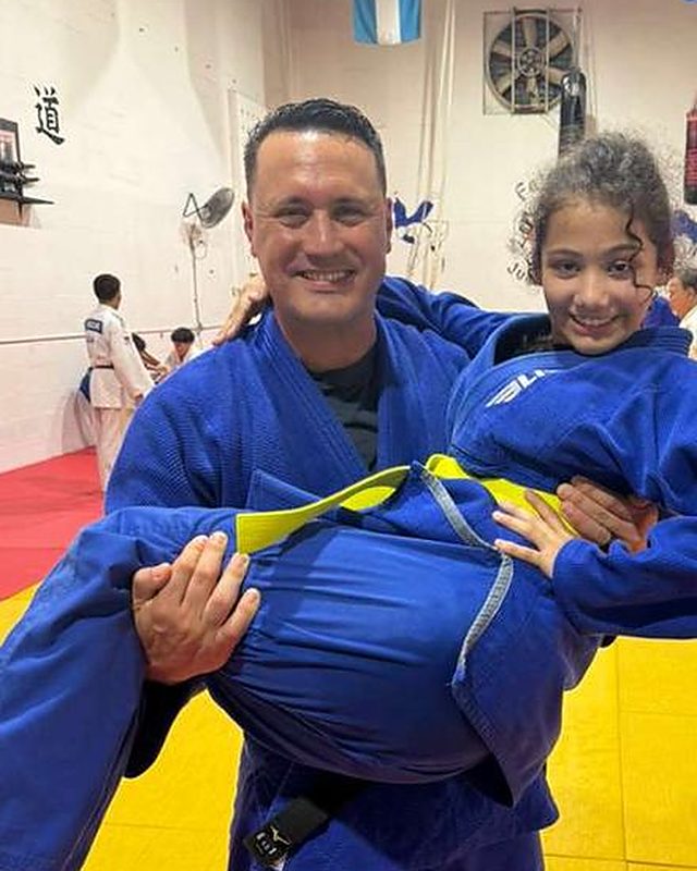 Sensei Omar Ojeda smiling and carrying a young student in a blue judogi.