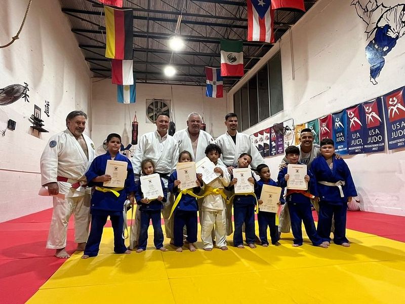 Kids holding their diplomas in the dojo with their coaches standing behind them.