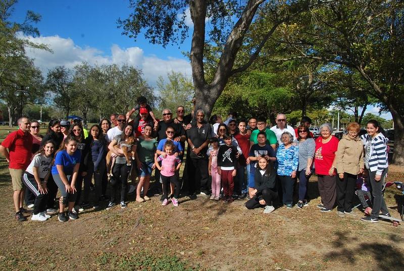 A large group of families and friends together outdoors in a park on a sunny day.